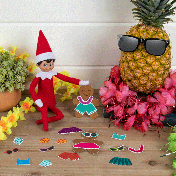 The Elf on the Shelf sitting on a table with printable paperdoll clothing and accessories for a merry and bright luau.  