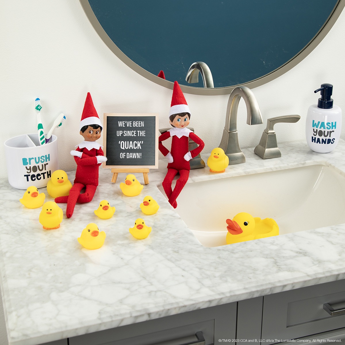 The Elf on the Shelf and friend sitting on a bathroom counter with rubber ducks and printable message card.