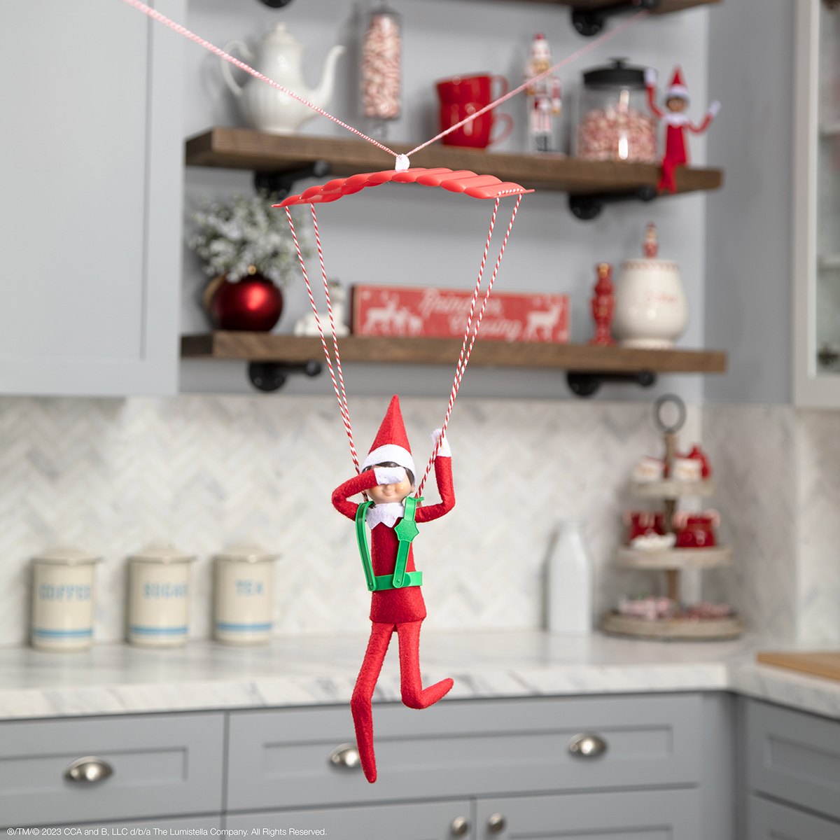 Alt text: The Elf on the Shelf ziplining through the kitchen while covering their eyes.