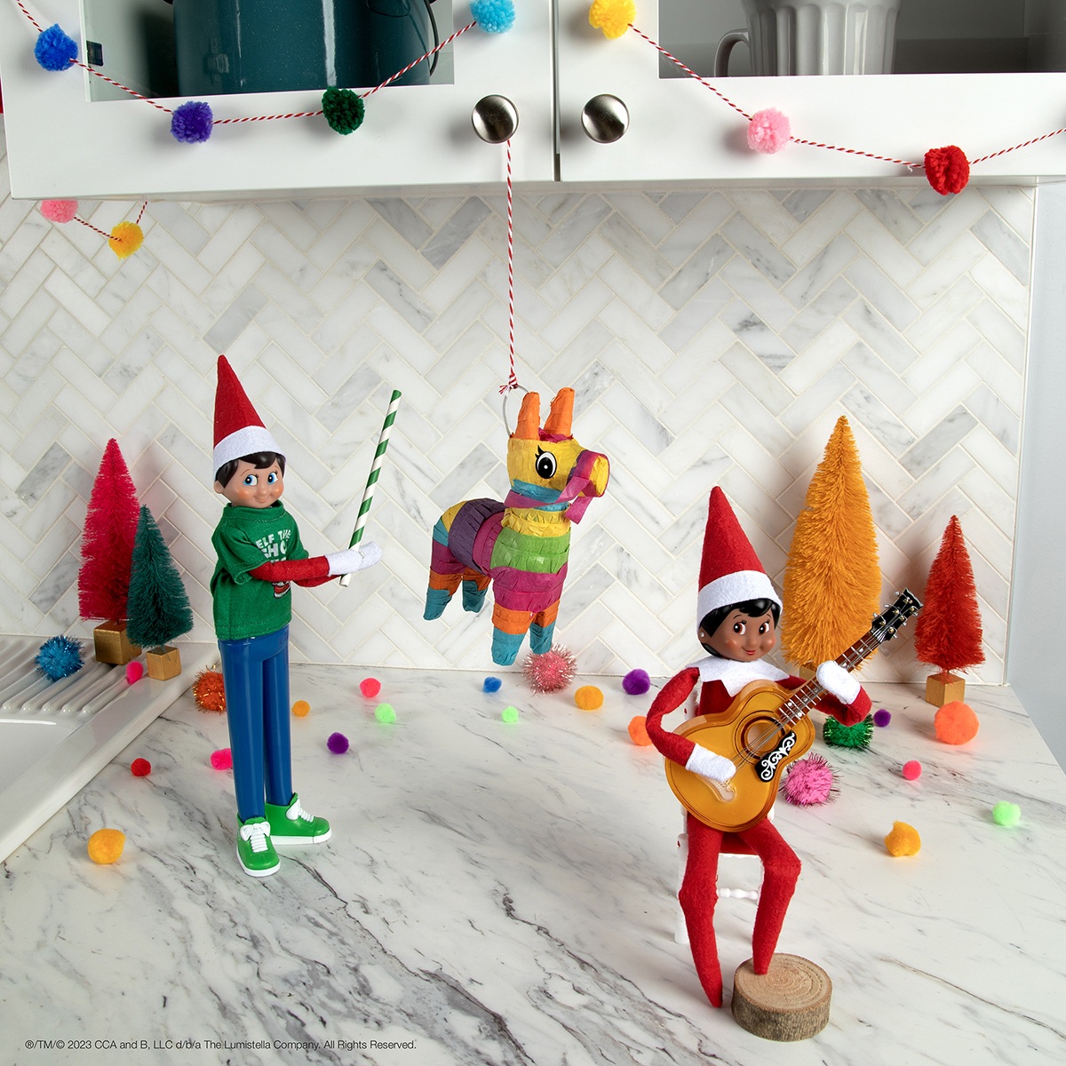 The Elf on the Shelf and friend swinging a small bat at a pinata and playing an elf-sized guitar.
