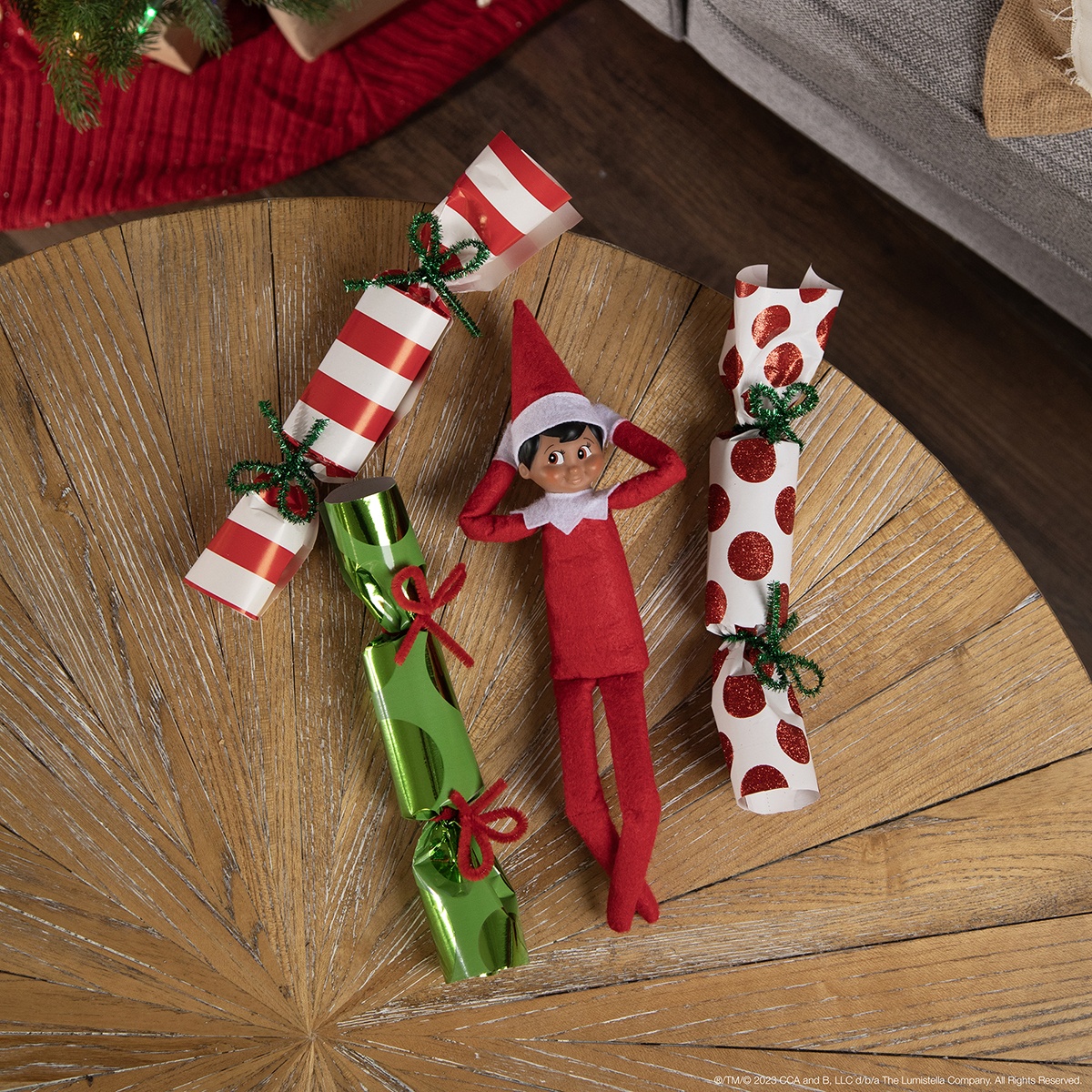 The Elf on the Shelf lying next to Christmas crackers with candies inside. 