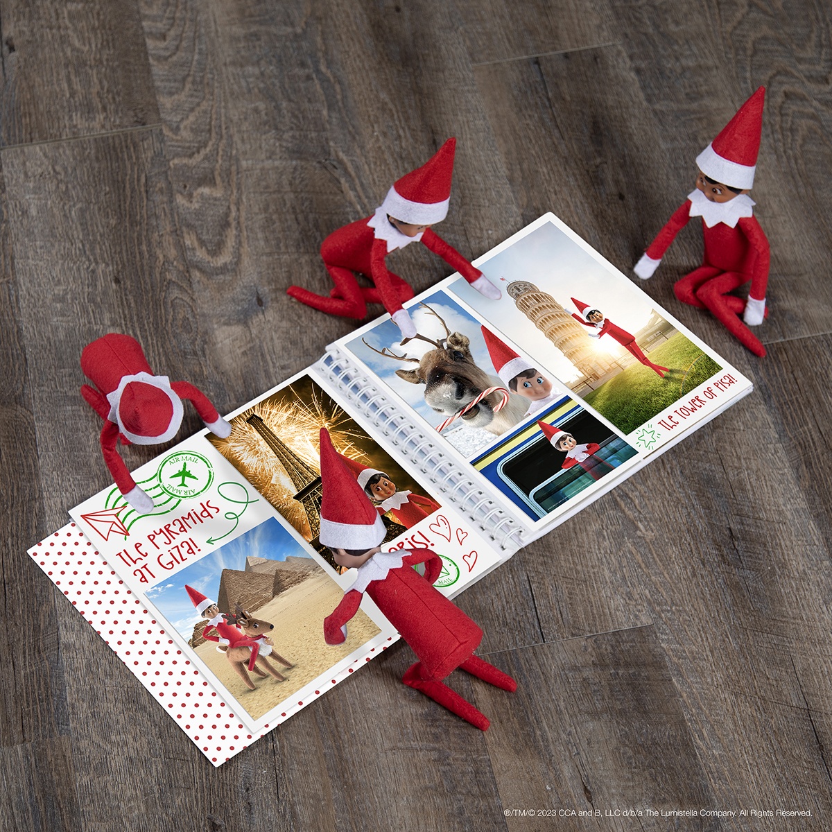 The Elf on the Shelf and friends looking through a scrapbook full of travel photos.
