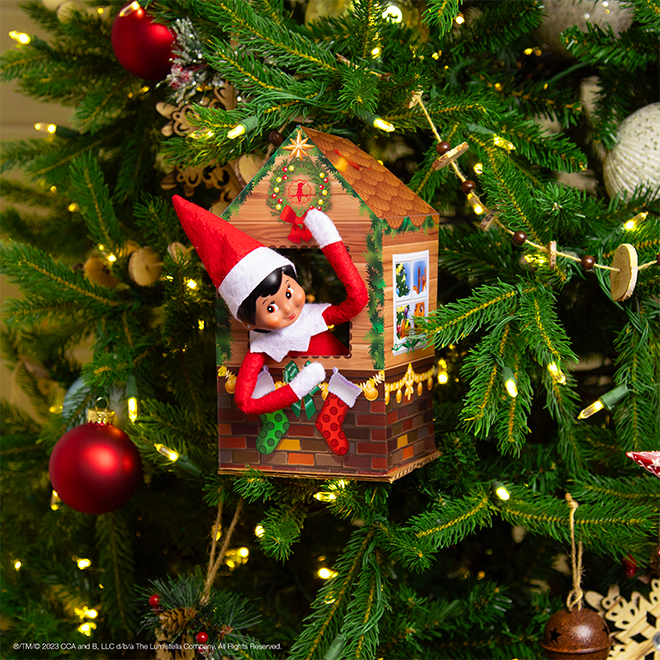 The Elf on the Shelf sitting in a printable tree house in a Christmas tree.