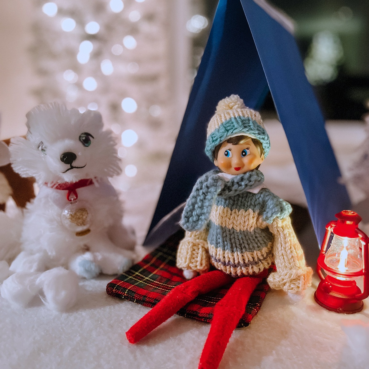 Scout Elf with a sweater and a hat sitting under a tent and next to the Elf Pets arctic fox and a lantern