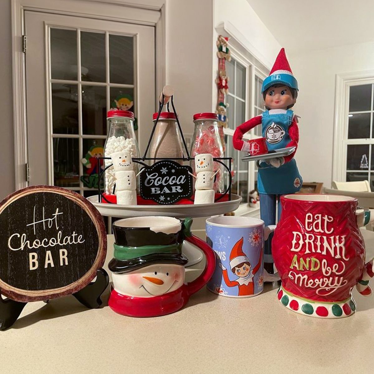 A Scout Elf standing next to hot cocoa ingredients and mugs