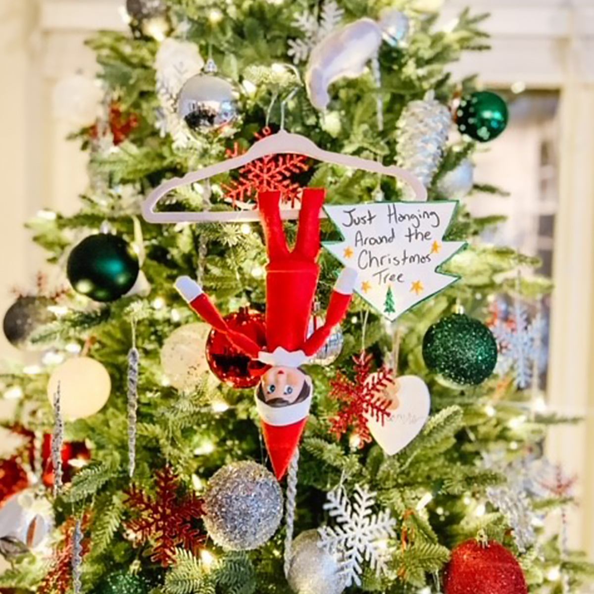 A Scout Elf hanging upside down on a hanger on a Christmas tree