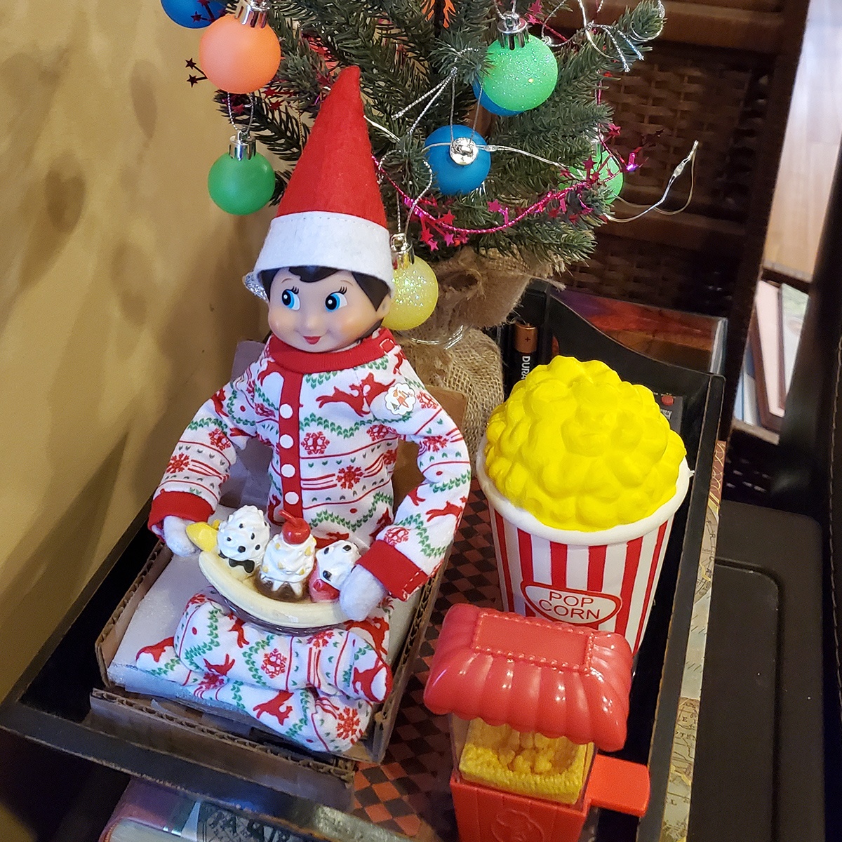 A Scout Elf wearing a blanket while holding an ice cream sundae next to popcorn