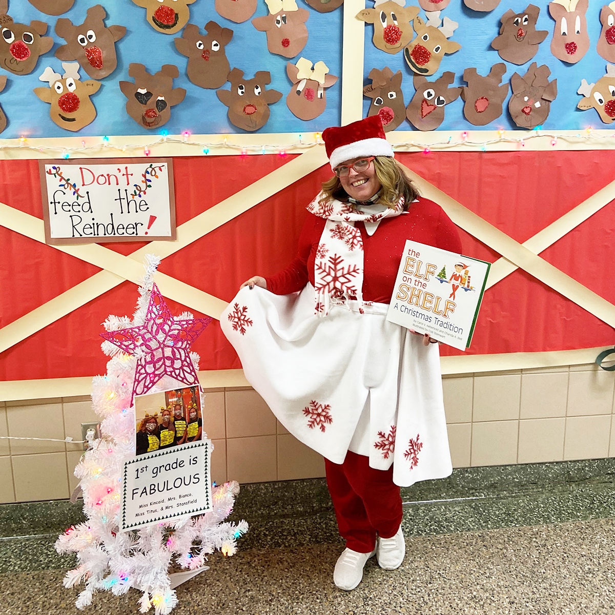 A teacher dressed as a Scout Elf holding The Elf on the Shelf book