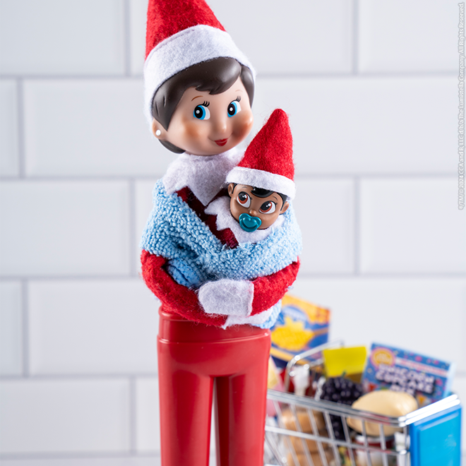 Scout Elf holds a Frost Pips baby at the grocery store