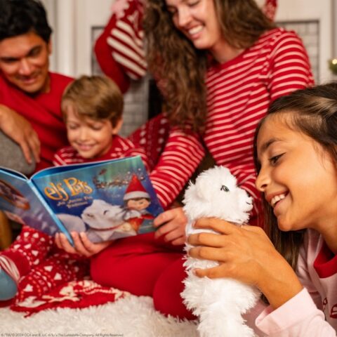 A mom, dad, son and daughter read the Elf Pets Arctic Fox Tradition storybook together while the girl cuddles with the arctic fox plush