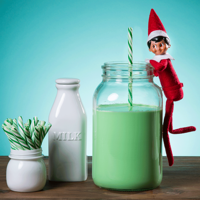 The Elf on the Shelf stirs a jar of green milk with a straw