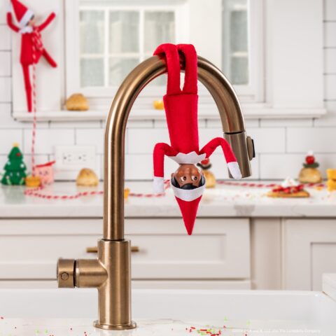 The Elf on the Shelf hangs upside down from the faucet over the kitchen sink