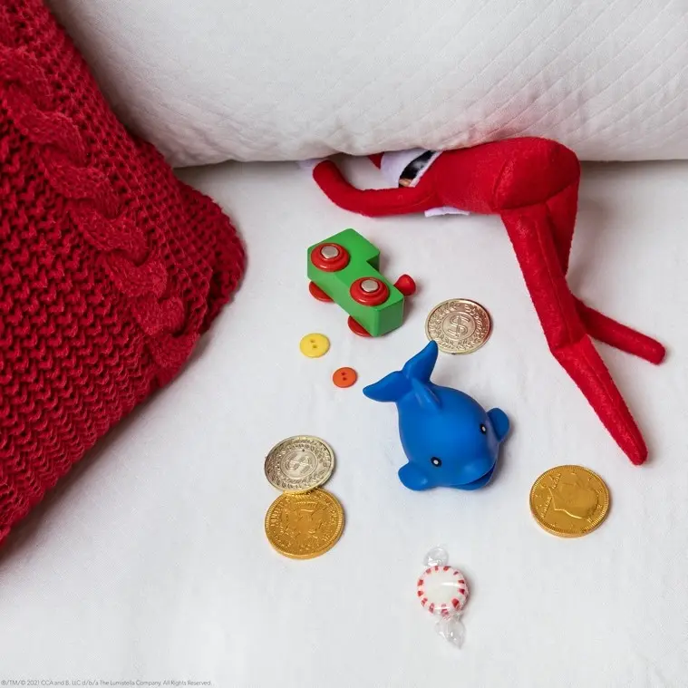 Scout Elf on sofa with head between cushions, coins and small toys are behind him as if he has found them in the sofa