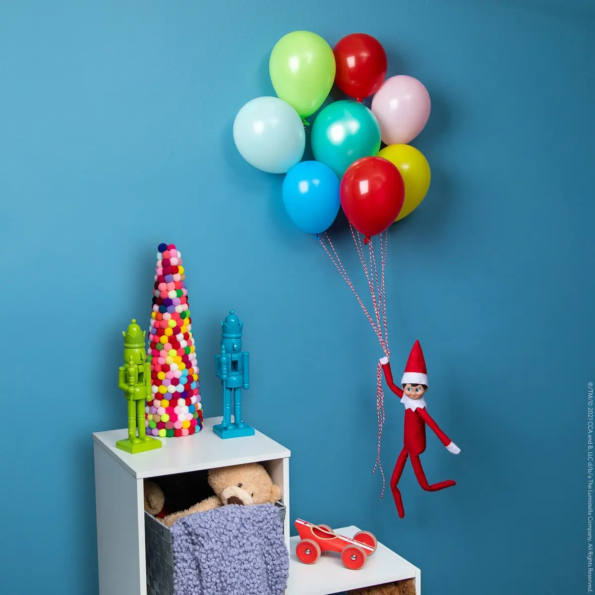 The Elf on the Shelf holds onto a bundle of balloons as it lifts him into the air