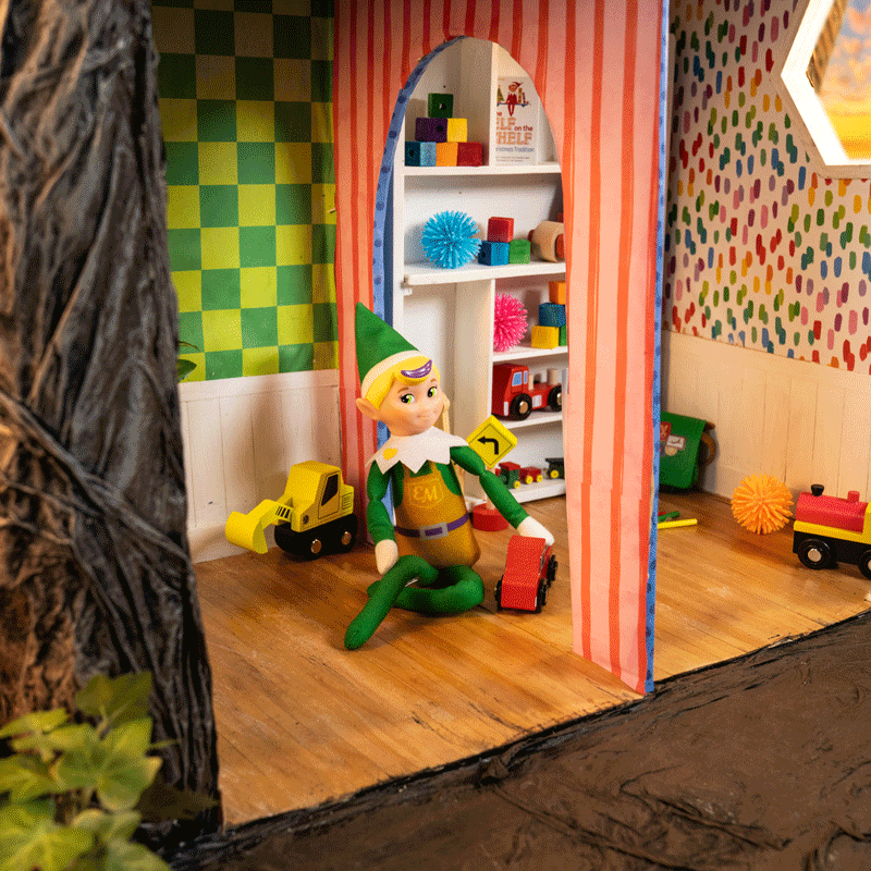 The Elf Mates Toy Maker sits in the toy workshop moving a toy car back and forth