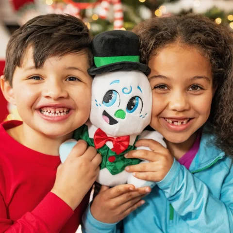 Young boy and girl smile while holding Razzle the Celebration Snowman plush between them