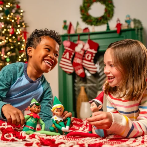 A young boy laughs and plays with the Elf Mates Cobbler and Toy Maker while a young girl holds the Elf Mates Girl Chef and smiles