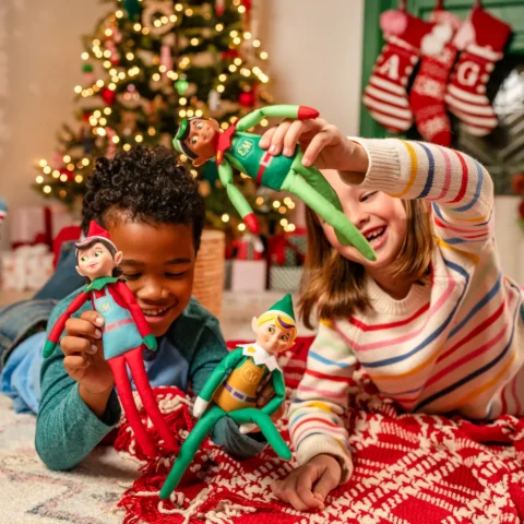 A boy and girl play with the Elf Mates while sitting on the floor in a living room decorated for kitchen