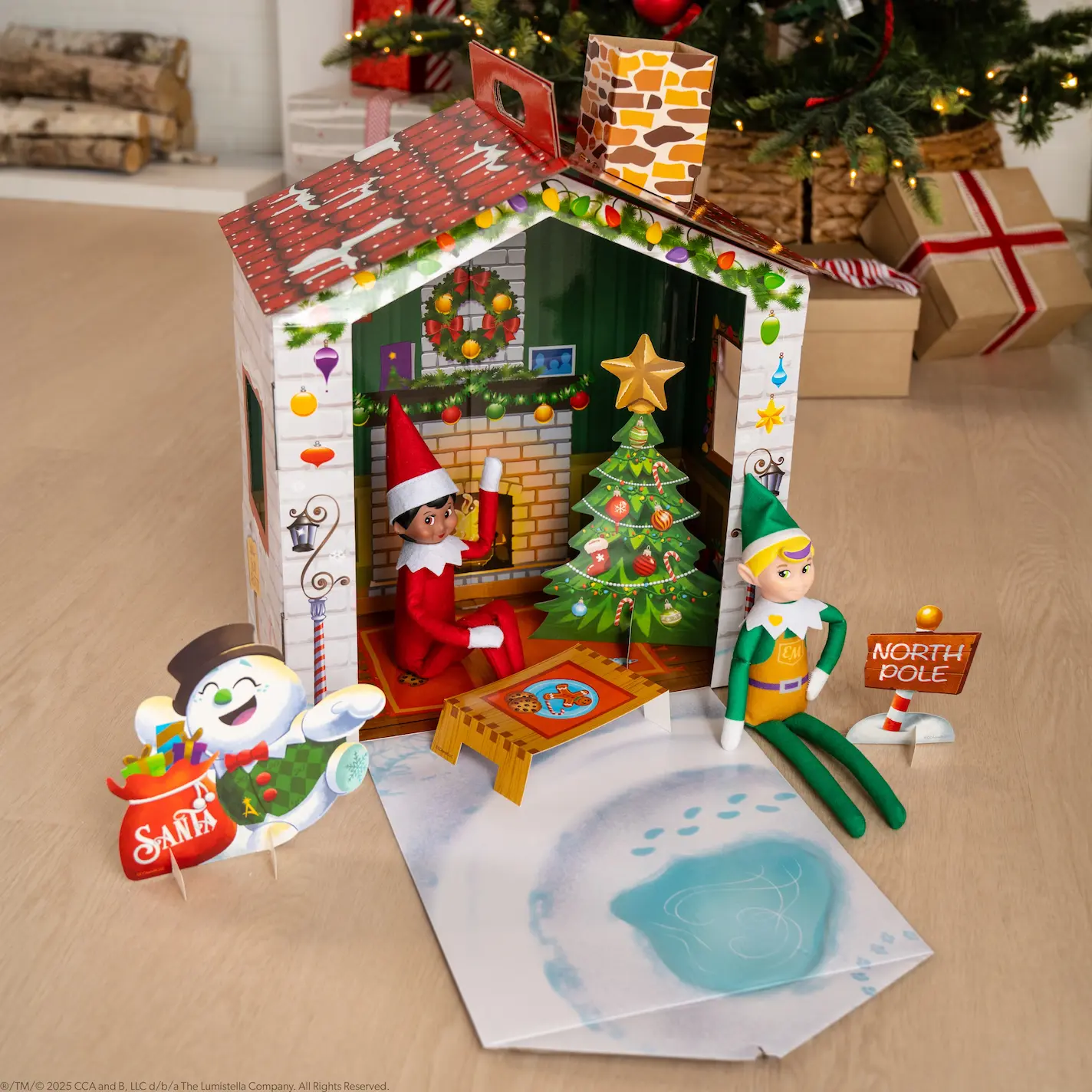 A decorative cardboard house with a Scout Elf and and Elf Mate sitting inside