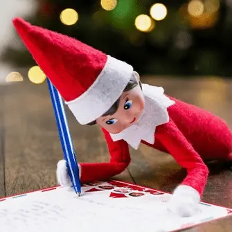 A Scout Elf lays on her stomach with pen in hand to write a letter