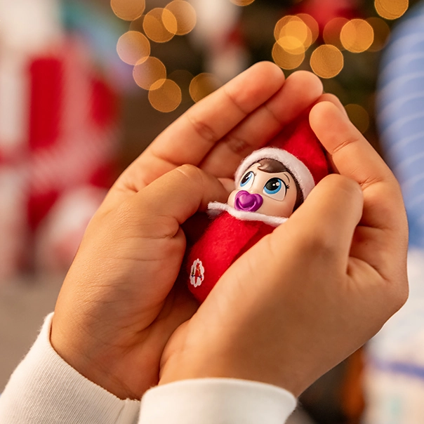 A child lovingly holds a Frost Pips™ girl with blue eyes in her hands with a slightly out of focus Christmas tree in the background. You can also make out the presents surrounding the tree.