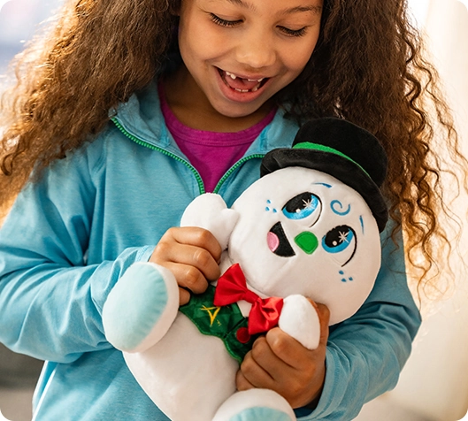 A little girl is holding the SnoStax™ Razzle the Snowman Plush with bright light pouring into the background. She is smiling and happy, clutching the plush in a joyous fashion.