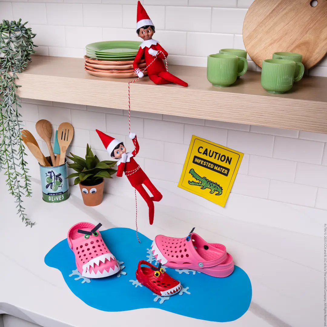 An elf holds a rope as another elf descends toward a pretend pond with crocodiles made of rubber shoes