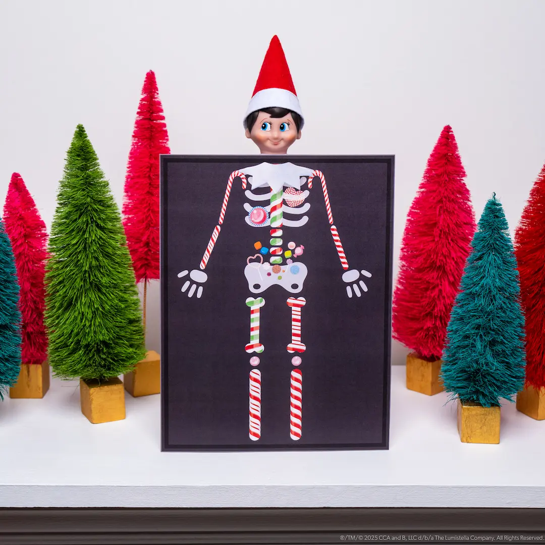 The Elf on the Shelf stands behind a printed paper that looks like an elf x ray image