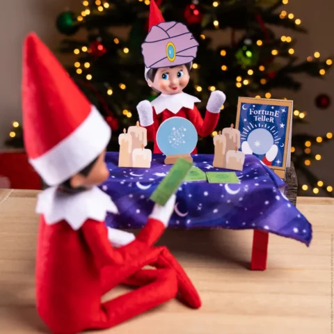 A Scout Elf dressed as a fortune teller faces another Scout Elf who sits at her table