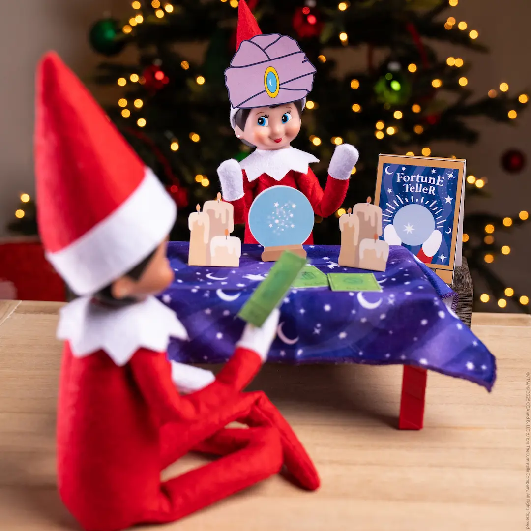A Scout Elf dressed as a fortune teller faces another Scout Elf who sits at her table