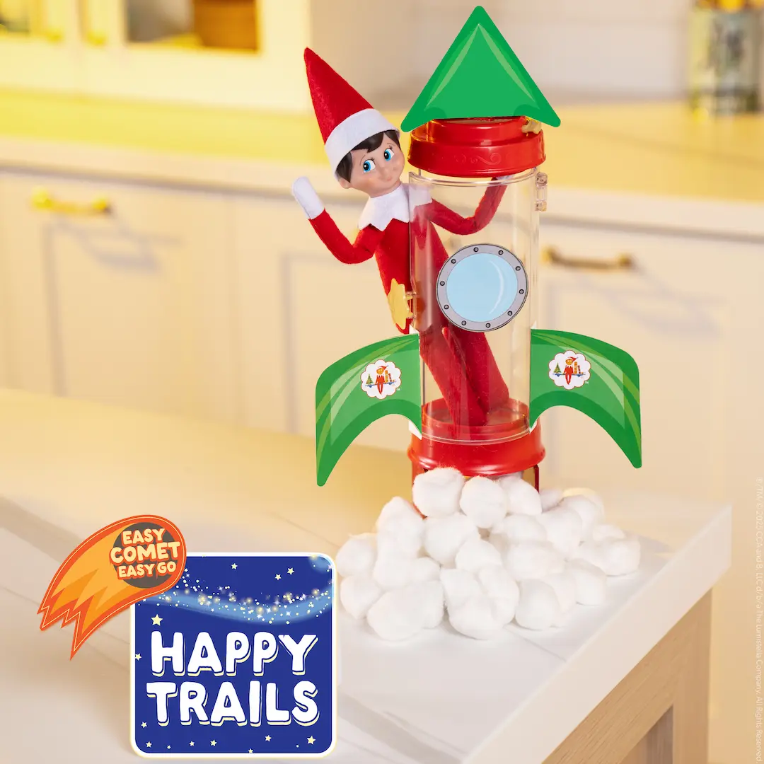 The Elf on the Shelf Scout Elf boy stands in an elf carrier that is decorated to look like a rocket