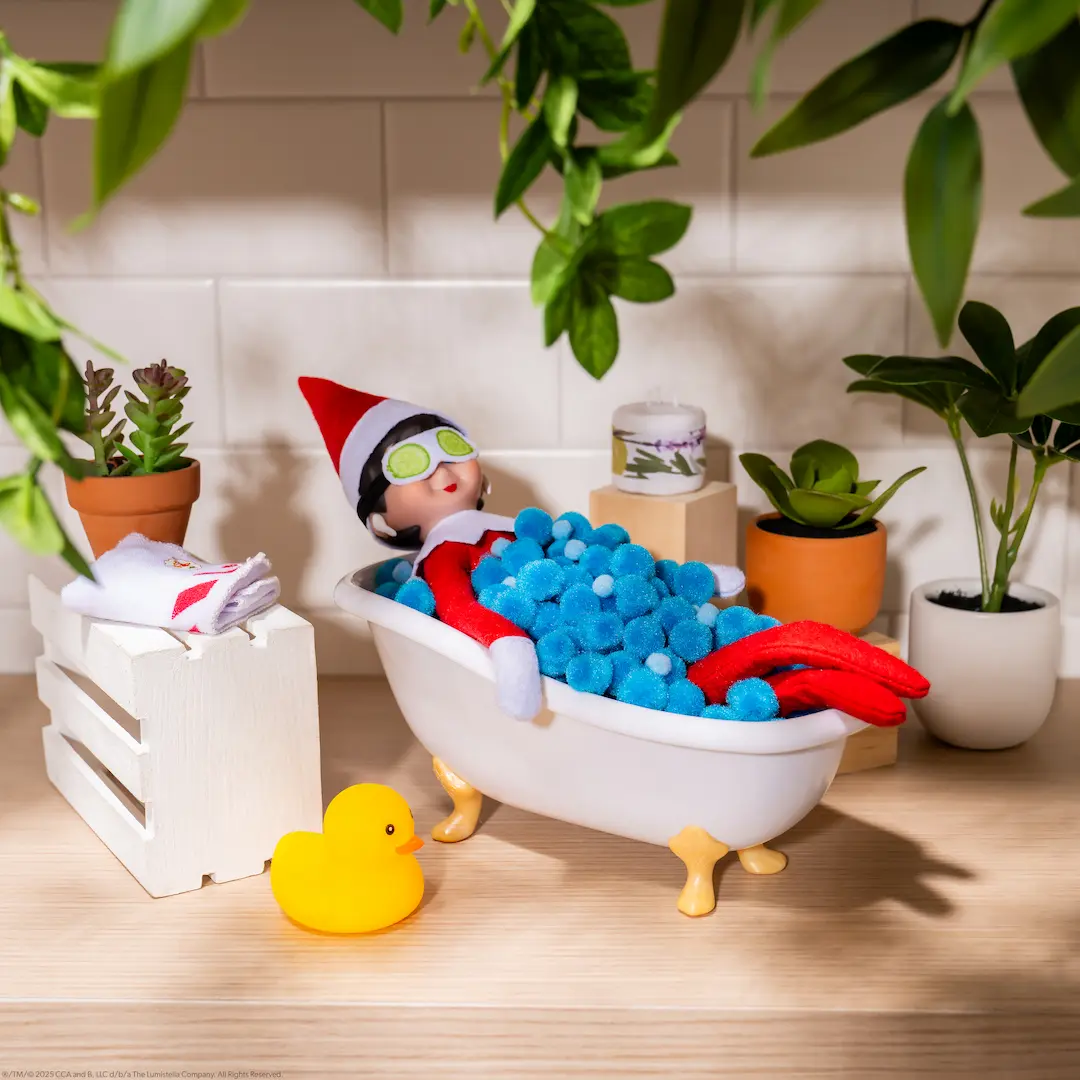 The Elf on the Shelf Scout Elf girl relaxes in a bathtub with a spa mask over her eyes
