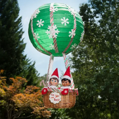 Two Scout Elves arrive in a hot air balloon with a sign that says "I'm back"