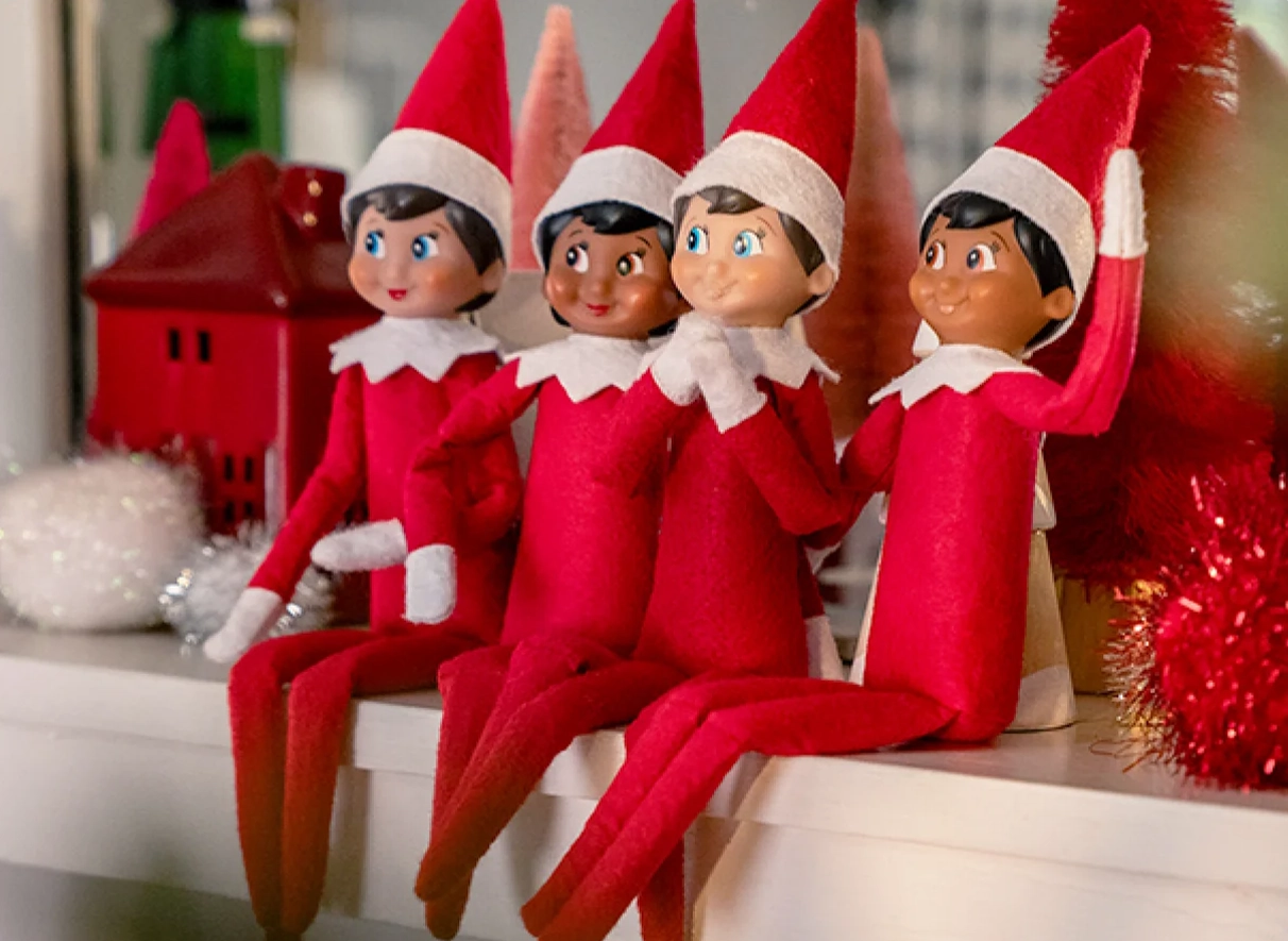 A grouping of Scout Elves sit atop a fireplace mantle. They are situated as a group hanging out and in different poses.