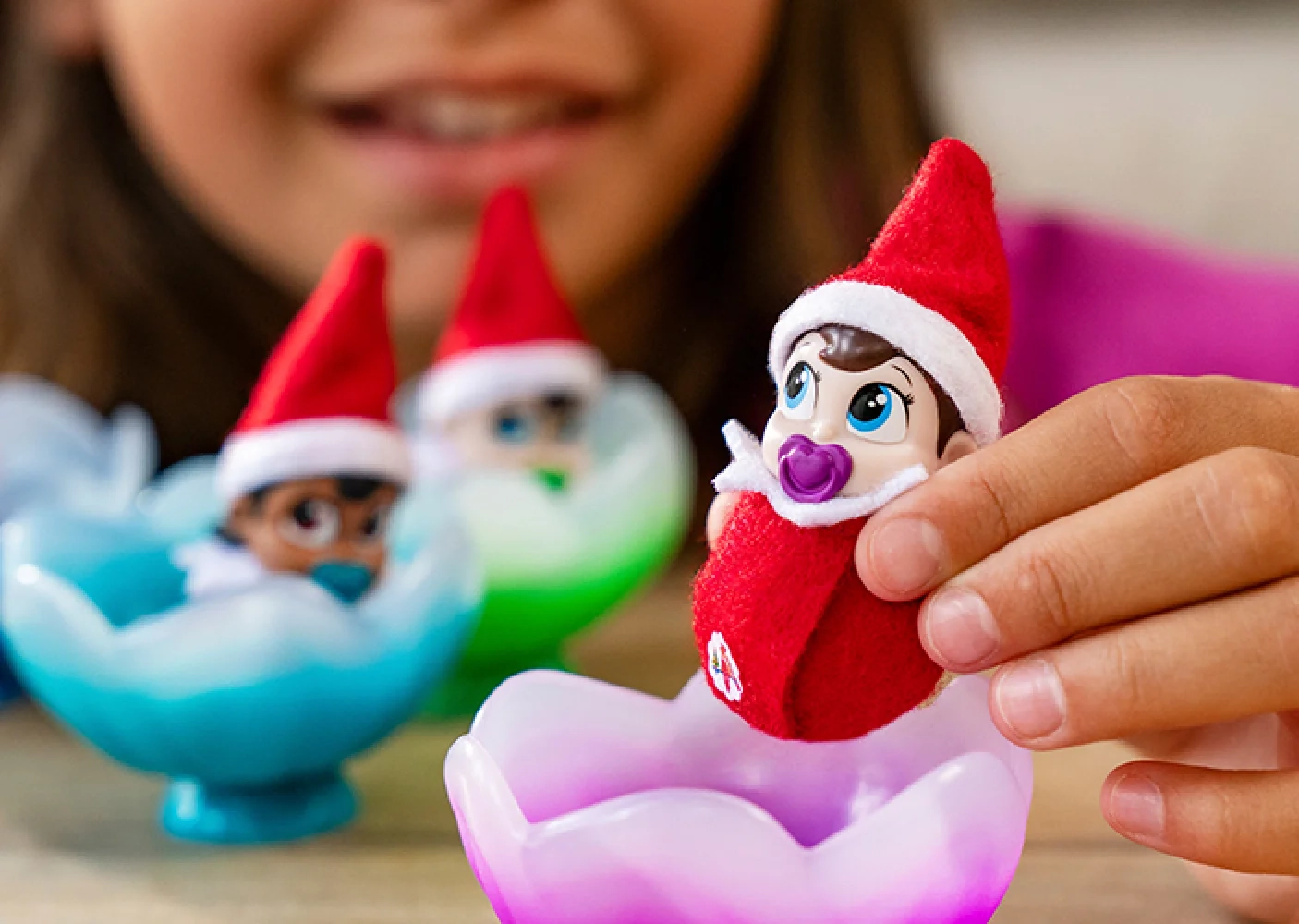 A young girl is gently picking up the Frost Pips™ Boy with Blue Eyes baby elf. You can make out the other Frost Pips™ in the background.