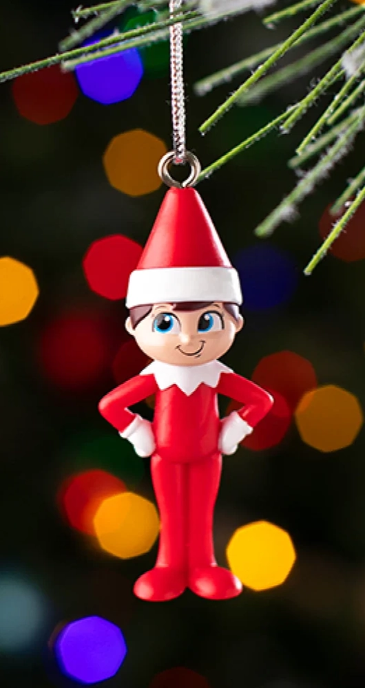 A close up shot of the Scout Elf ornament from the Santaverse™ Ornament Collection. You can see pine needles toward the top of the image, indicating that it is hanging on a Christmas tree. Blurred out in the background are some colored Christmas lights.