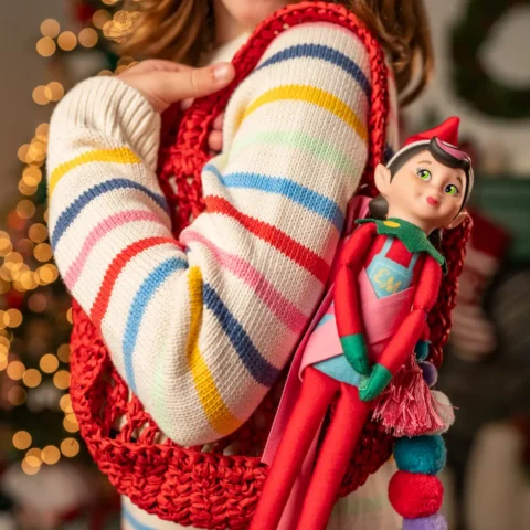A young girl in a striped sweater holds a red bag with an Elf Mates girls chef tied as a bag charm