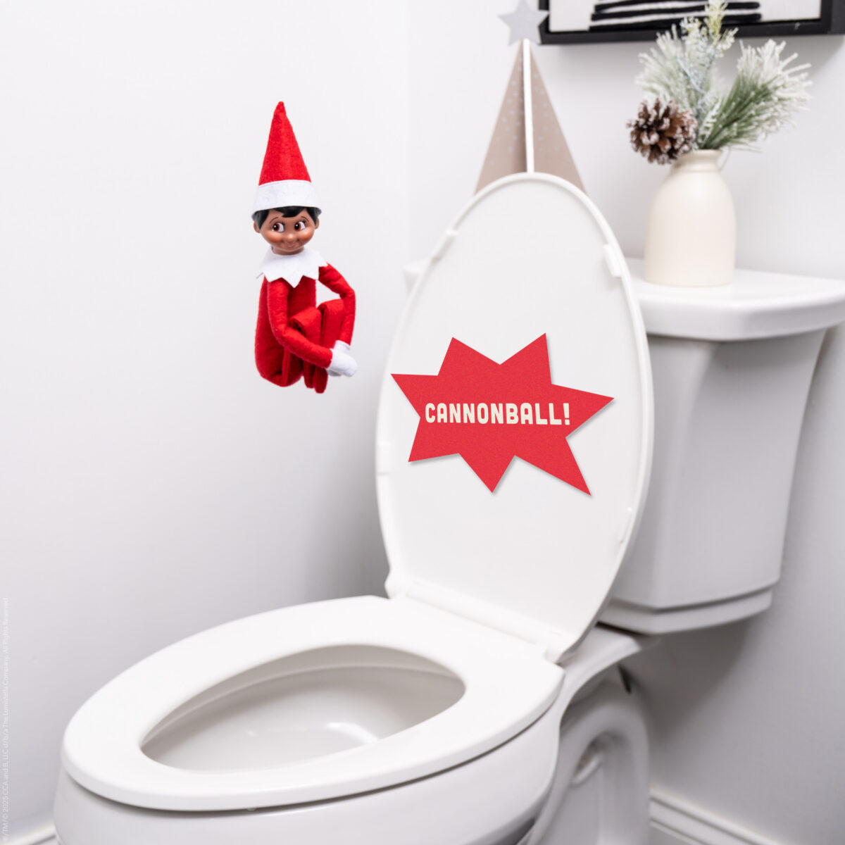 The Elf on the Shelf is suspended mid-air over the toilet as if about to jump into a pool with a sign that says CANNONBALL!