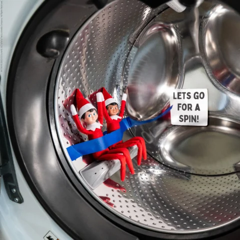 Scout Elf on the Shelf sitting inside an open dryer drum with a “Let’s Go for a Spin” sign, pretending to ride a rollercoaster.