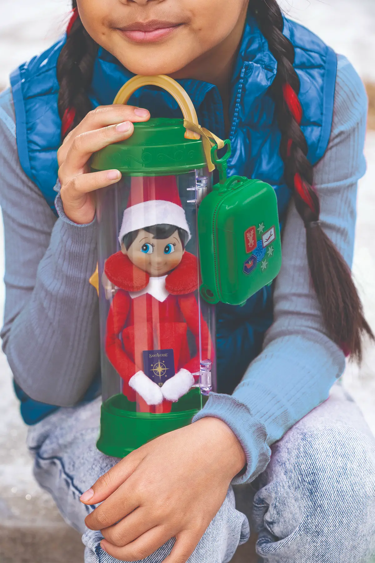 A girl in braids holds the green Scout Elf carrier with her Elf on the Shelf safely inside