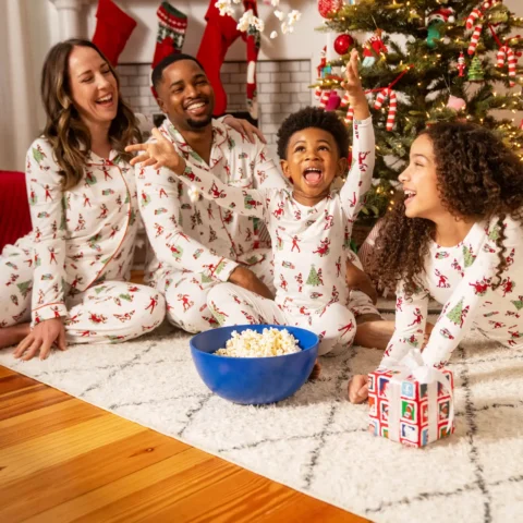 A family with two children celebrates Christmas while eating popcorn and laughing with The Elf on the Shelf in the backgrund