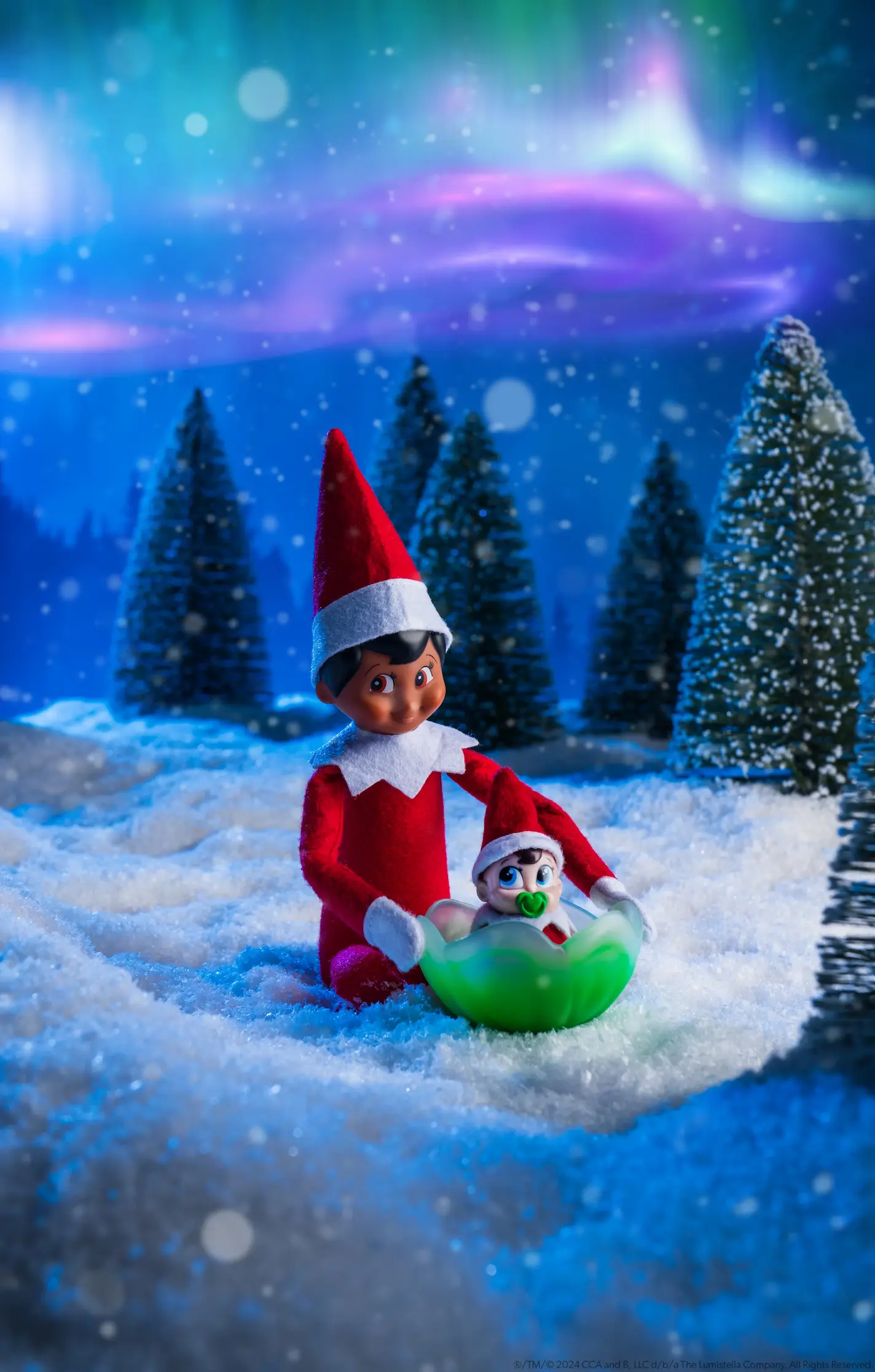 A grown Elf on the Shelf Scout Elf cares for a Frost Pips Scout Elf baby at the North Pole