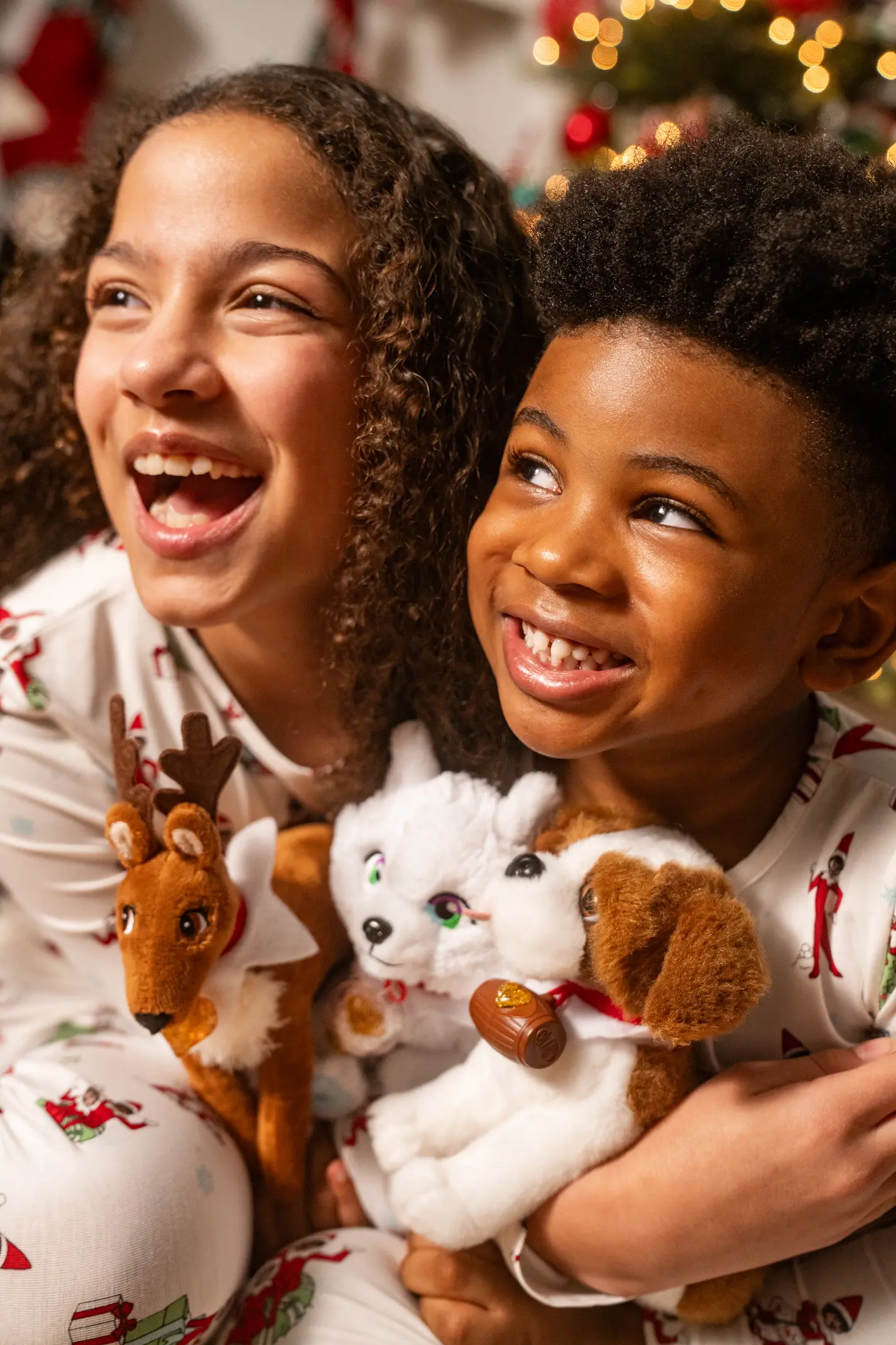 A boy and a girl hold the three Elf Pets plush with big smiles on their faces