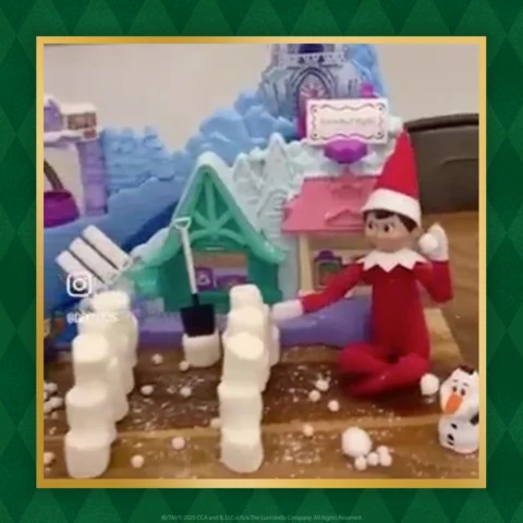 The Elf on the Shelf sits in front of rows of marshmallows that make a pathway to a toy castle