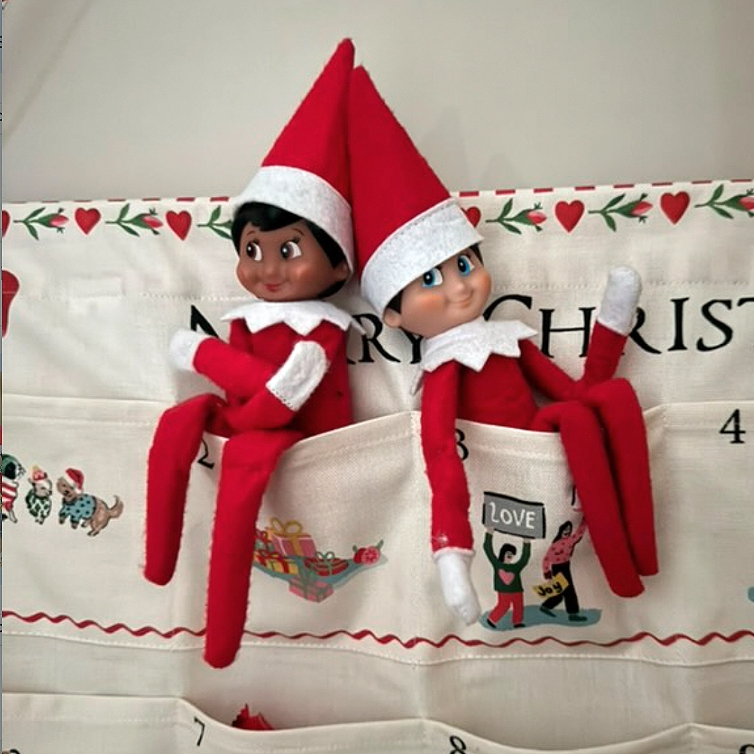 A pair of Scout Elves are hanging out in an advent calendar. The advent calendar is made of fabric with sewn in pockets, where they are resting.