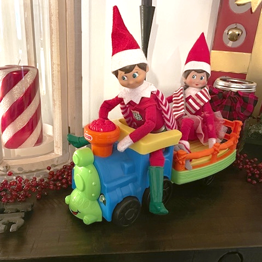 A pair of Scout Elves are taking a ride on a plastic, colorful, toy train!