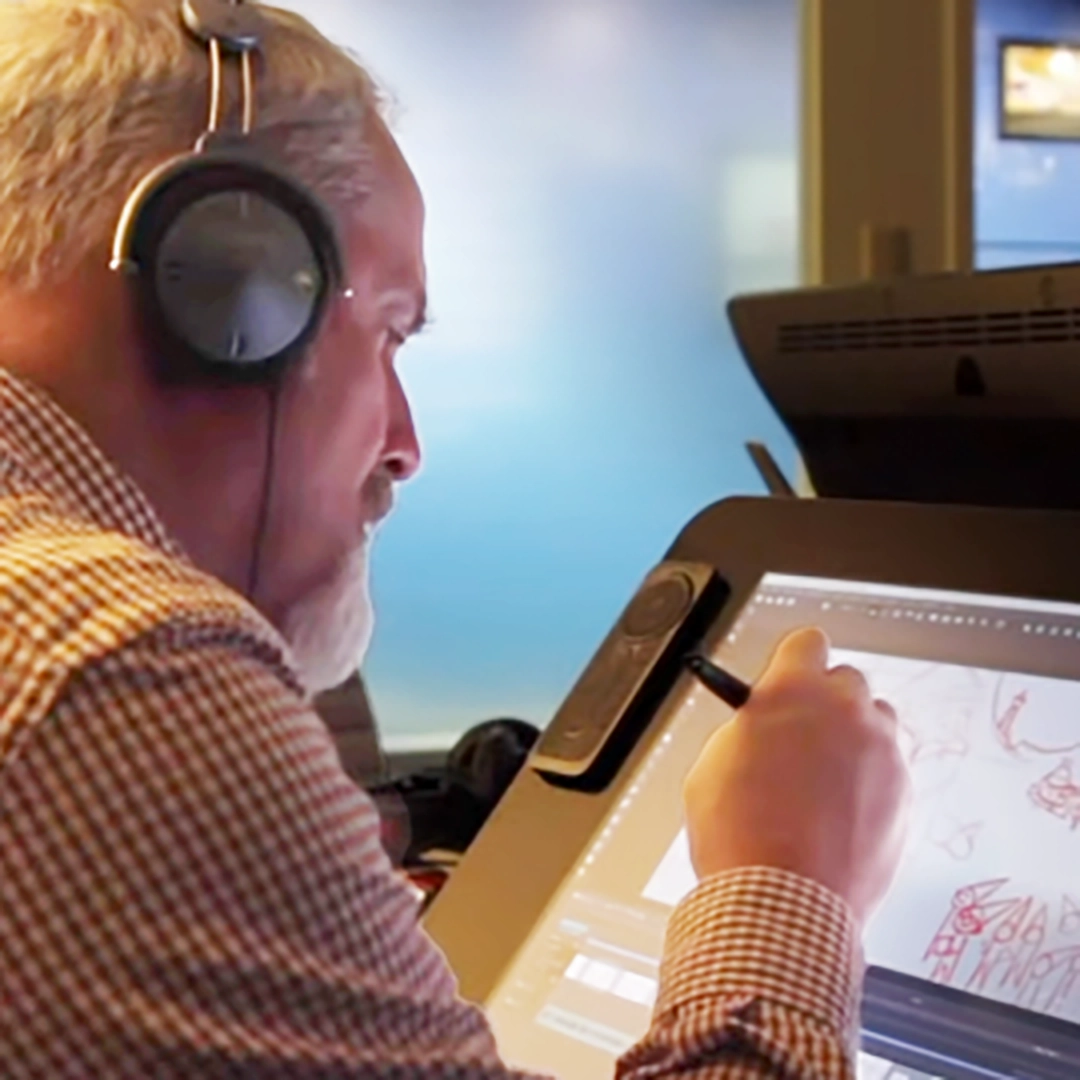 An animator works on the Elf Pets: Santa's Reindeer Rescue animated special. He wears a set of over-the-ear headphones and is concentrating on his work, displayed on a Wacom drawing tablet with pen in hand.