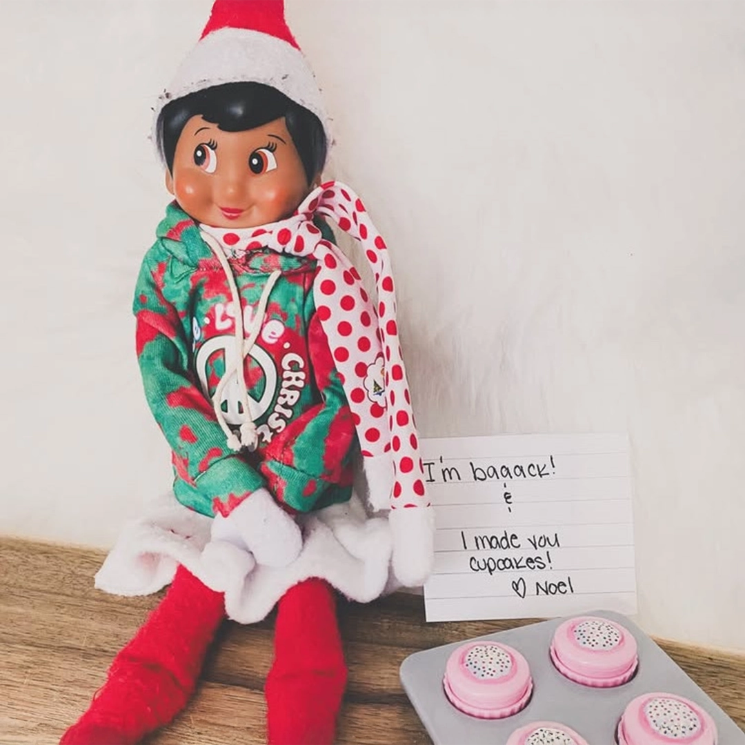 A female Scout Elf is sporting a Claus Couture groovy hoodie and scarf, with a note that reads, "I'm baaack! & I made you cupcakes! Love, Noel". There are also the Poler Props cupcakes shown.