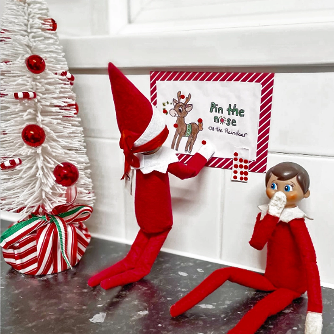 A pair of Scout Elves play a friendly round of "Pin the Nose on the Reindeer" hanging on the wall.