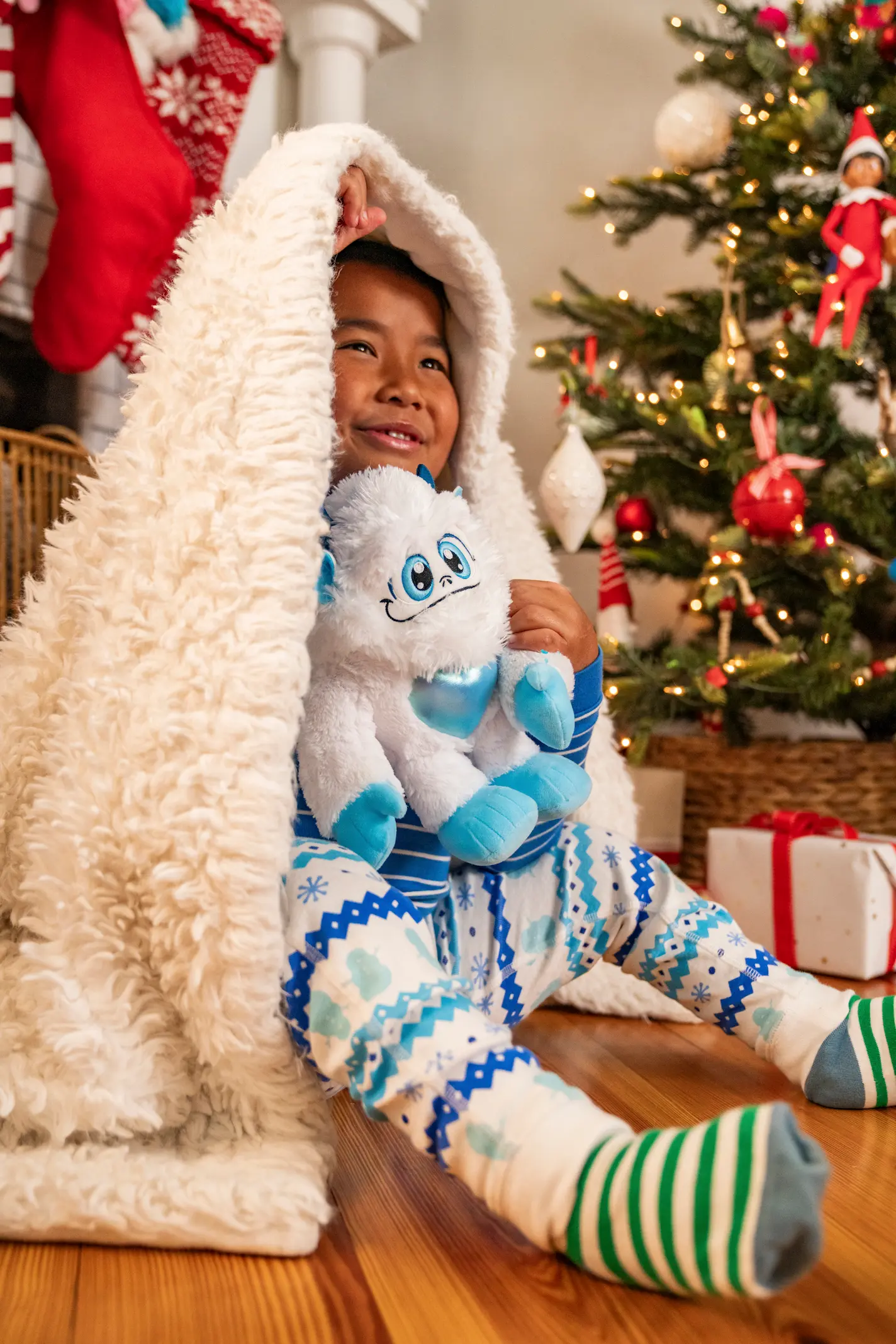A boy holds the Little Grunt SnoBiggie plush while hiding under a white blanket